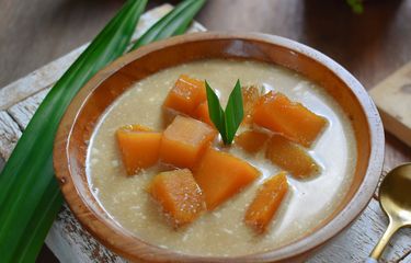 Bubur Labu Kuning Tradisional: Seporsi Bubur Labu Kuning dengan warna cerah, disajikan dengan kuah santan kental dan gula merah yang manis